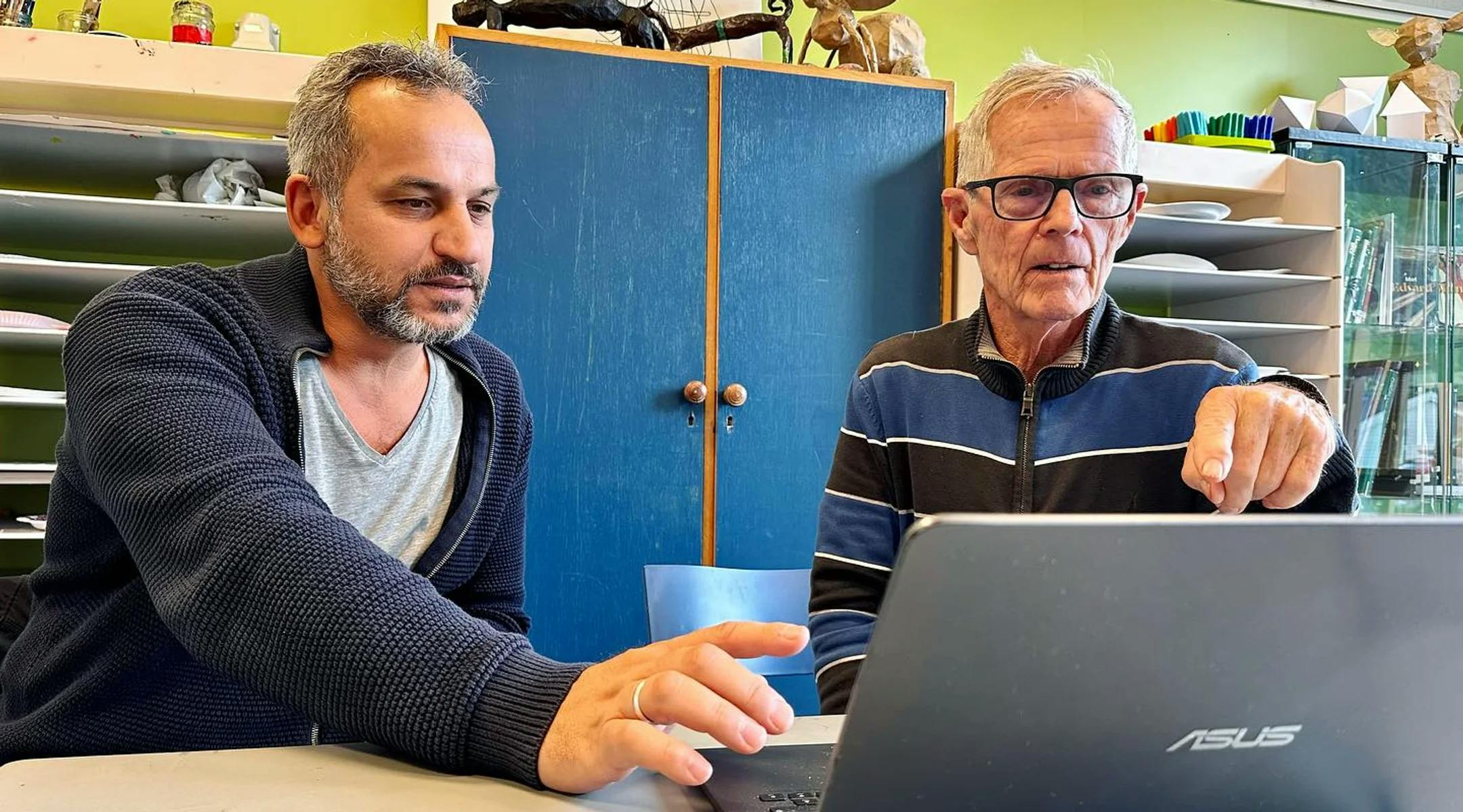 En mannlig frivillig fra Haugesund Røde kors hjelper en eldre mann med noe på PCen
